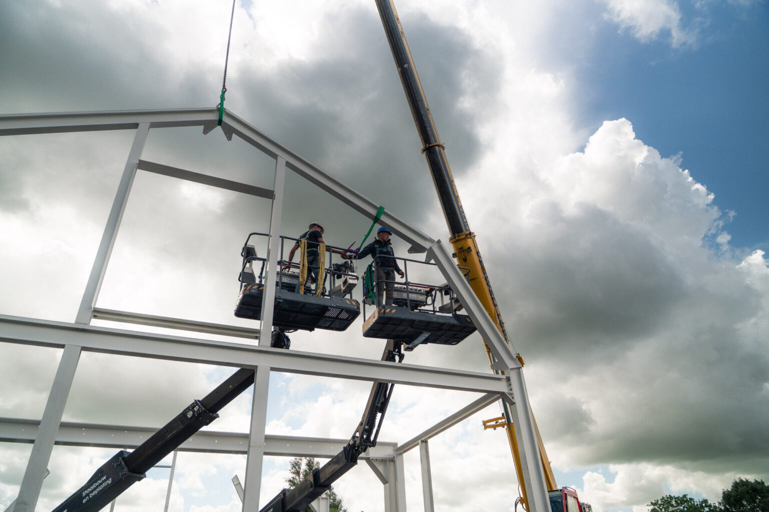 Twee monteurs werken vanuit hoogwerkers aan de staalconstructie
