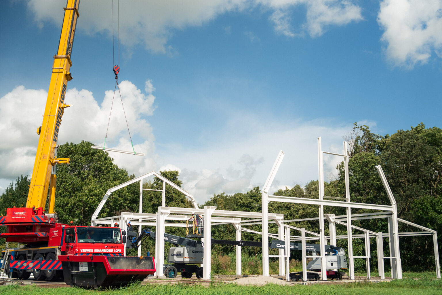 Mobiele kraan hijst een spant boven de staalconstructie in aanbouw